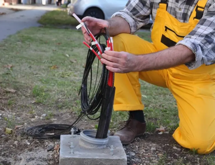A fiber internet technician kneels on the ground to install fiber cable to an outdoor connection box.
